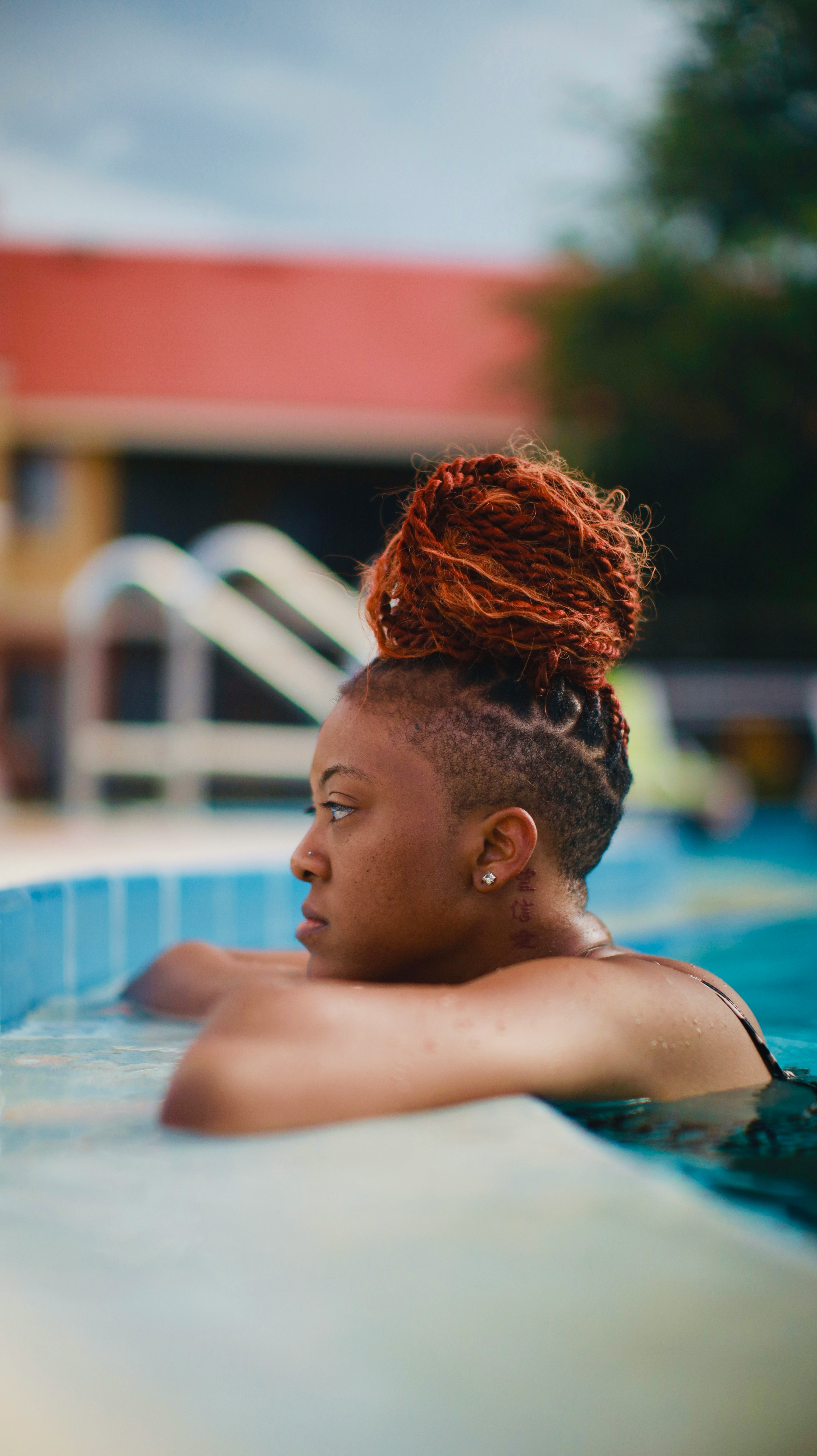 Profile portrait of a woman with red braided hair, resting at the edge of a pool.