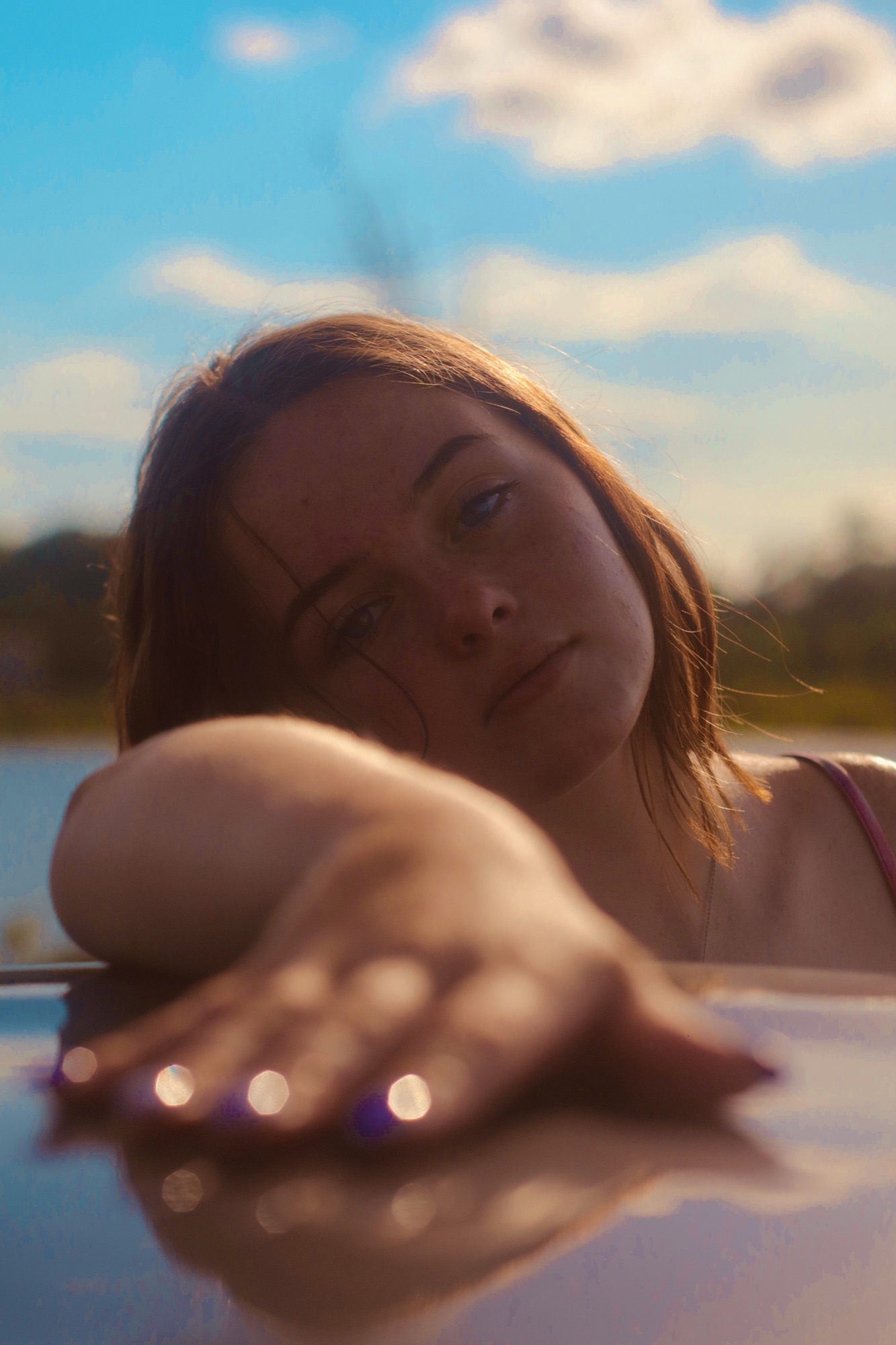 Woman reaching a hand toward the camera at golden hour beside a lake.