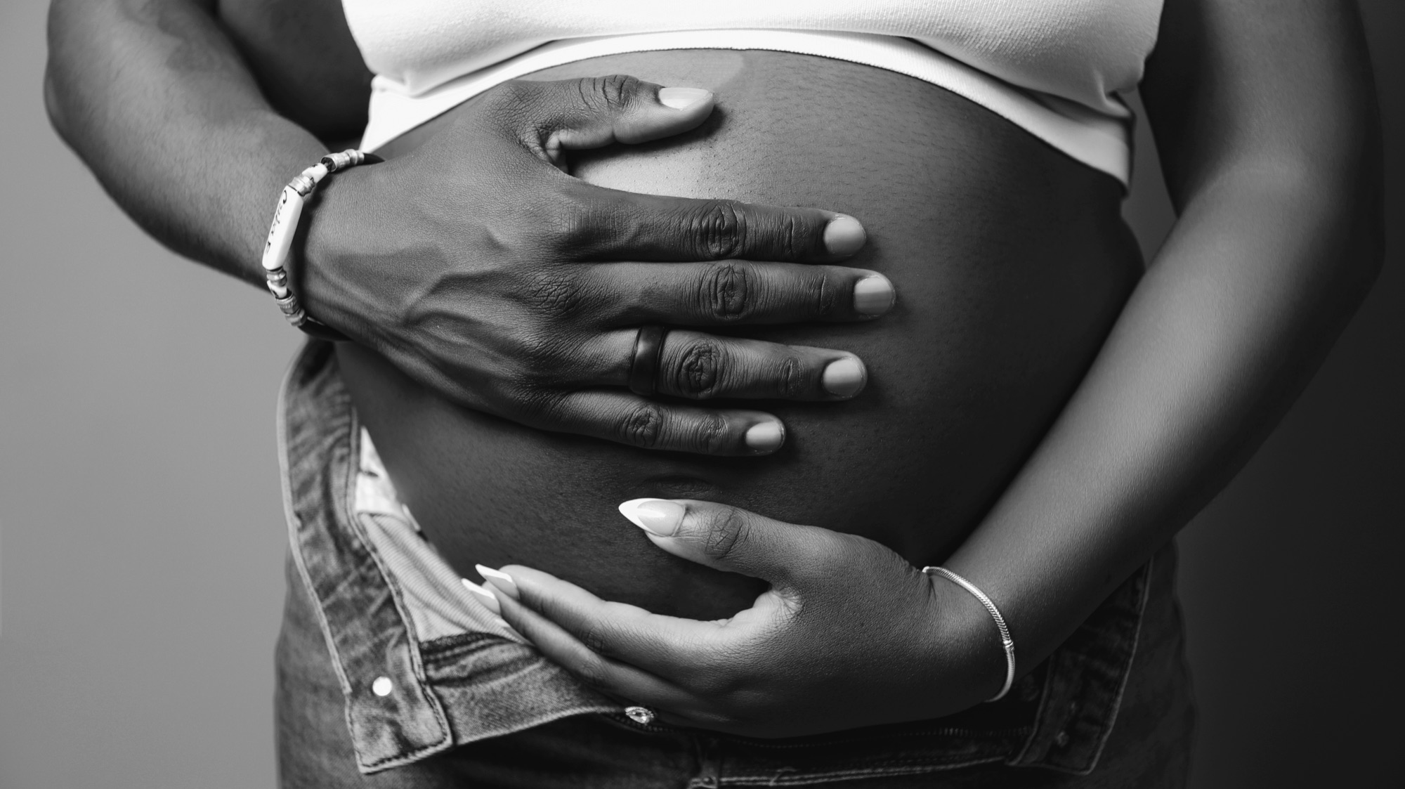 Black-and-white close-up of hands resting on a pregnant belly.